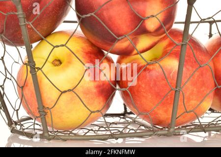 Several juicy organic nectarines in a wire basket, close-up, isolated on white. Stock Photo