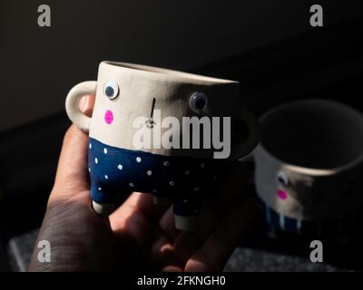 Cute face ceramic plant pot in hand. Close-up hand holding small modern DIY cement planters trendy decoration. Stock Photo