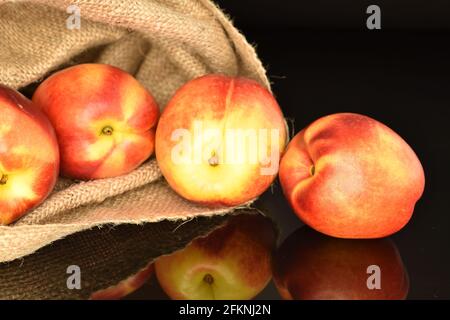 Several fresh nectarines with a jute bag, close-up, on a black background. Stock Photo
