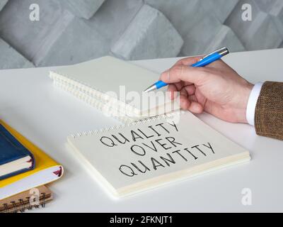 Man writes phrase quality over quantity on the page. Stock Photo