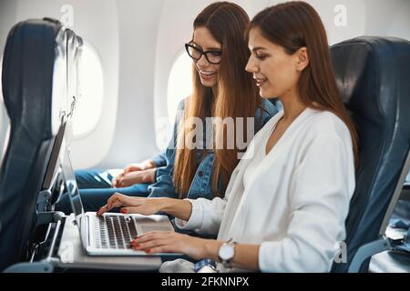 Two gladsome ladies using laptop in the plane Stock Photo