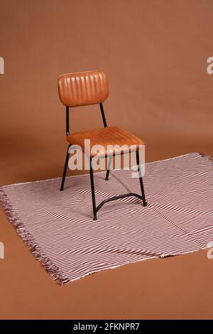 Black metal and brown leather chair on a carpet of red and white lines with a brown background. Stock Photo