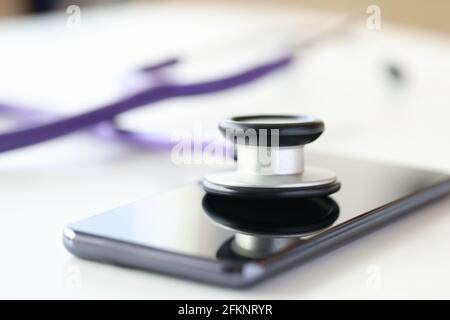 Medical instrument stethoscope lying on screen of mobile phone closeup Stock Photo