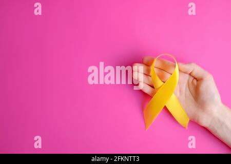 Woman's hand holding yellow ribbon - bladder, liver and bone cancer awareness symbol. Children cancer prevention concept. Isolated background, copy sp Stock Photo