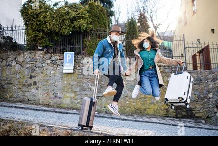 Young couple tourists with luggage walking and jumping on streets in old town, coronavirus concept. Stock Photo