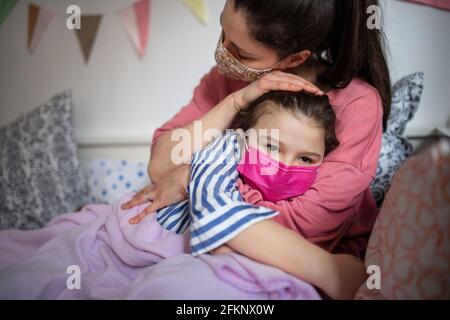 Tired mother looking after sick small daughter in bed at home, coronavirus concept. Stock Photo