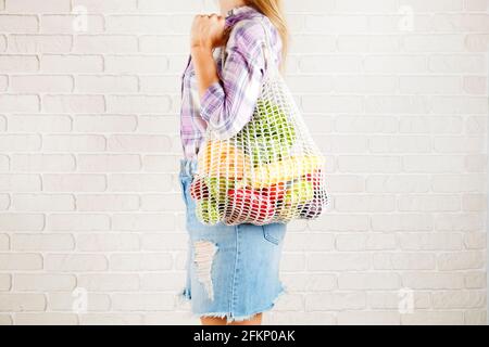 Young woman in plaid shirt, jeans skirt with bag of mixed fruit, vegetables: corn cob, tomato, pepper, lettuce salad, pear & apple. Zero waste concept Stock Photo