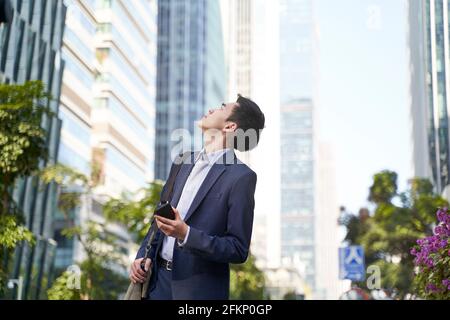 young corporate executive looking up at skyscrapers while walking in street in downtown of modern city Stock Photo