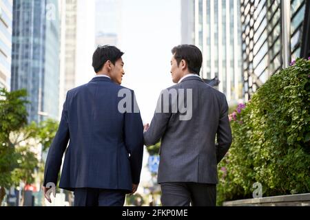 rear view of two asian corporate executives discussing business while walking in street in downtown of modern city Stock Photo