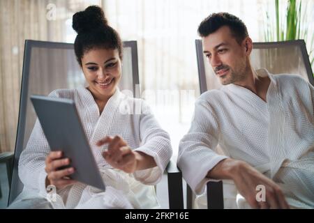 Portrait of young couple relaxing in spa resort, using tablet. Stock Photo