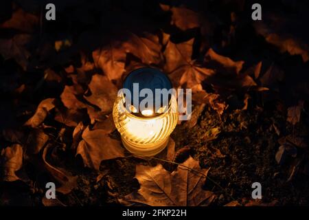 Single candle light on the ground at night, surrounded by autumn leaves. Stock Photo