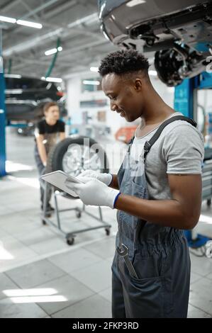 Mechanic using laptop, car on lift, auto service Stock Photo