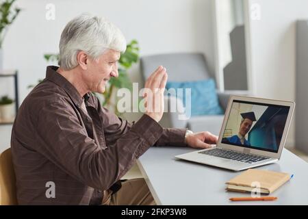 Side view of mature man watching teenage son graduating by video chat Stock Photo