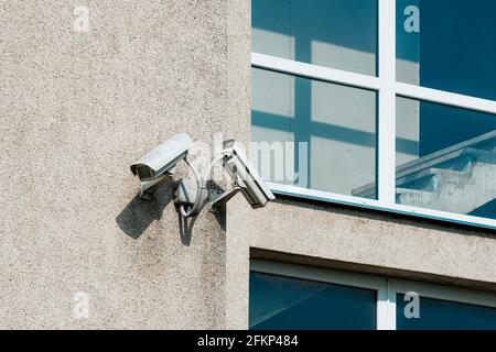 Two CCTV cameras on grey building wall with big windows Stock Photo