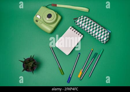 Notebook, pens and instax camera on green background  Stock Photo