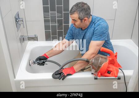 Man using a mini plumbers snake to unclog a bathtub drain Stock Photo