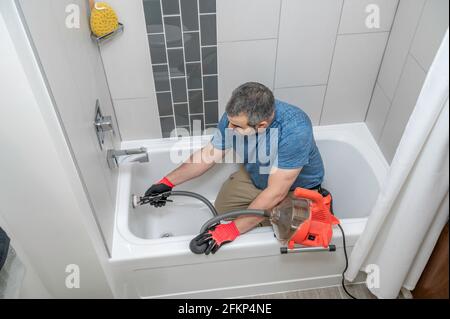 Plumber drain cleaning a bathtub with a plumbers snake Stock Photo