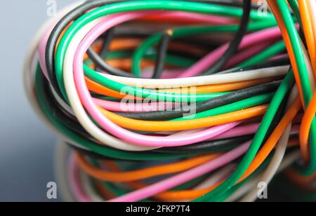 A bundle of multicolored electrical, car, computer, telephone wires twisted together background. Orange, green, pink, white cables on grey background Stock Photo