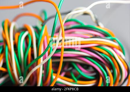 A bundle of multicolored electrical, car, computer, telephone wires twisted together background. Orange, green, pink, white cables on grey background Stock Photo