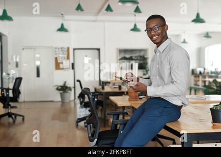 African businessman smiling while using a tablet at his office desk Stock Photo
