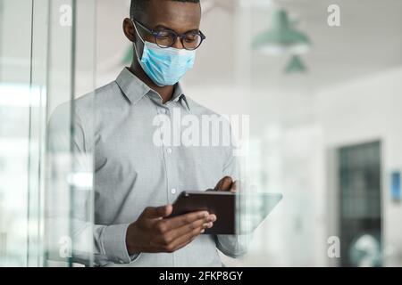 African businessman wearing a face mask using a digital tablet Stock Photo
