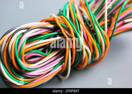 A bundle of multicolored electrical, car, computer, telephone wires twisted together background. Orange, green, pink, white cables on grey background Stock Photo