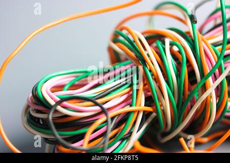 A bundle of multicolored electrical, car, computer, telephone wires twisted together background. Orange, green, pink, white cables on grey background Stock Photo