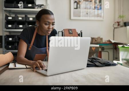African female leather worker using a laptop at a workbench Stock Photo