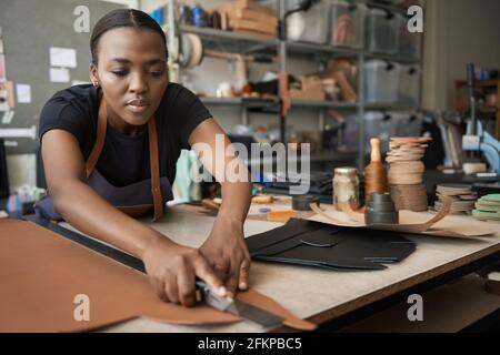 Young African female leather worker cutting leather at a bench Stock Photo
