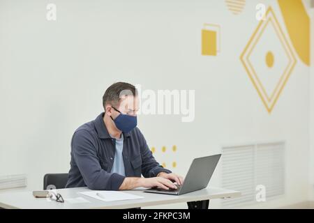 Portrait of mature college professor wearing mask while using laptop in modern school auditorium, copy space Stock Photo