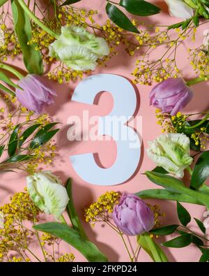 Number three on pink background with colorful flowers. Flat lay, top view. Stock Photo