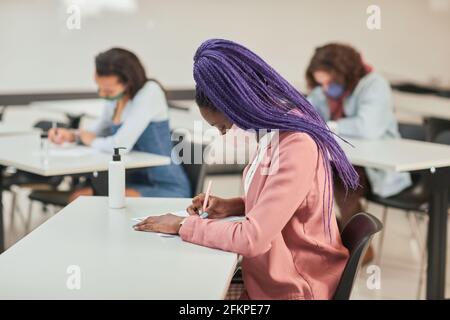 Side view portrait of young African-American woman wearing mask while taking test or exam in school with diverse group of people, copy space Stock Photo