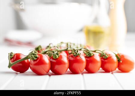 Fresh red cherry tomatoes. Small tomatoes on branch on white table. Stock Photo