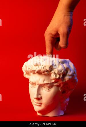 Plaster pot in the form of David's head and male hand on a red background. Stock Photo