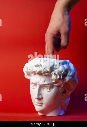 Plaster pot in the form of David's head and male hand on a red background. Stock Photo