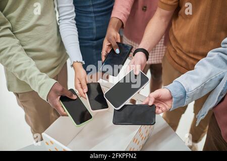 Top view closeup of diverse group of teenagers putting smartphones in box in no gadget classroom at school, copy space Stock Photo