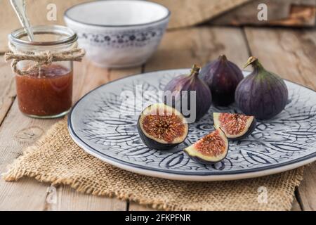 Figs on a blue and white patterned plate and a glass with fig jam on rustic jute and wood Stock Photo