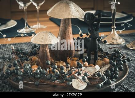 Autumnal table decoration with wooden mushrooms, berry wreath, hazelnuts and a wooden deer, dominated by dark blue, silver and wood colors Stock Photo