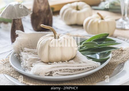 Place setting on a wooden table with white mini pumpkins, sage leaves and wooden mushrooms for Thanksgiving Day or Halloween Stock Photo
