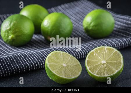 Lime halves on black background, in the background whole limes on a black tea towel Stock Photo