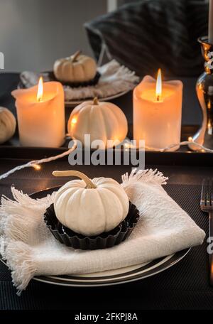 Place settings in black and white decorated with white pumpkins and white candles, vertical stock photo Stock Photo