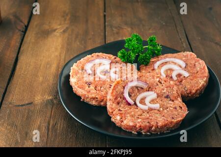 Three raw homemade burger meatballs with red onions on a black plate, copy space Stock Photo