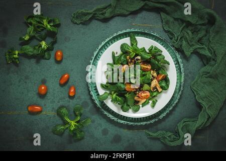 Fresh corn salad with mushrooms and roasted seeds on a white plate on green background, top view