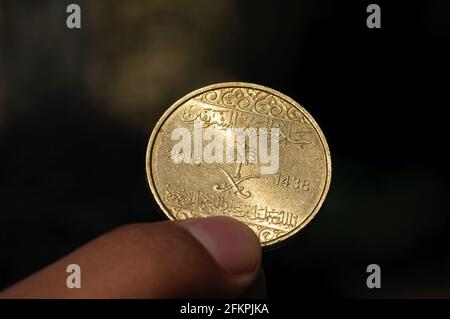 Asian child's hand holding a Fifty Halalas Riyal coin, Saudi Arabia money, selected focus and dark background Stock Photo