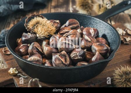 Roasted chestnuts in a cast iron pan on a wooden board Stock Photo