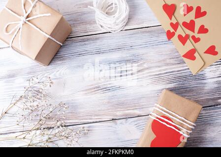 Gifts packed in craft paper, envelope, rope, paper hearts on a white wooden background, eco friendly home present decoration, top view, close up. Stock Photo