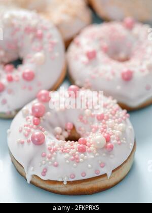 Delicious tender donuts glazed white glaze and sprinkled with pink pearl dressing. Idea decorating donuts for wedding, romantic event, celebration. Selective focus with copy space. Vertical Stock Photo