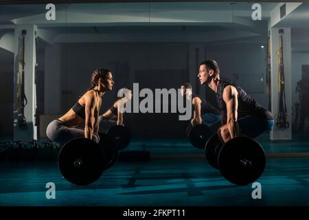 A female and a male training together and simultaneously doing dead-lift exercise at the gym. Stock Photo