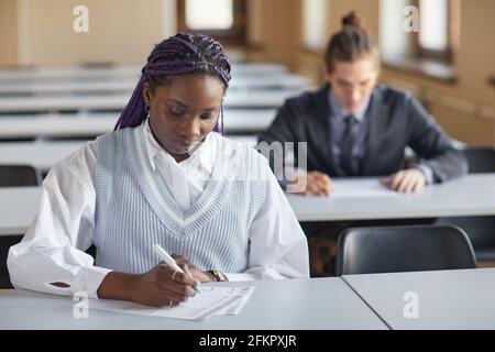 Portrait of young African-American woman wearing school uniform while taking exam in college auditorium, copy space Stock Photo