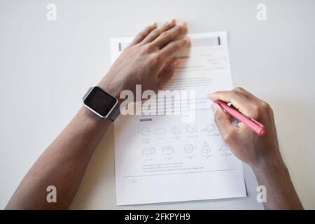 Top view closeup of unrecognizable African-American boy writing in notebook while taking math test in school, focus on smartwatch, copy space Stock Photo